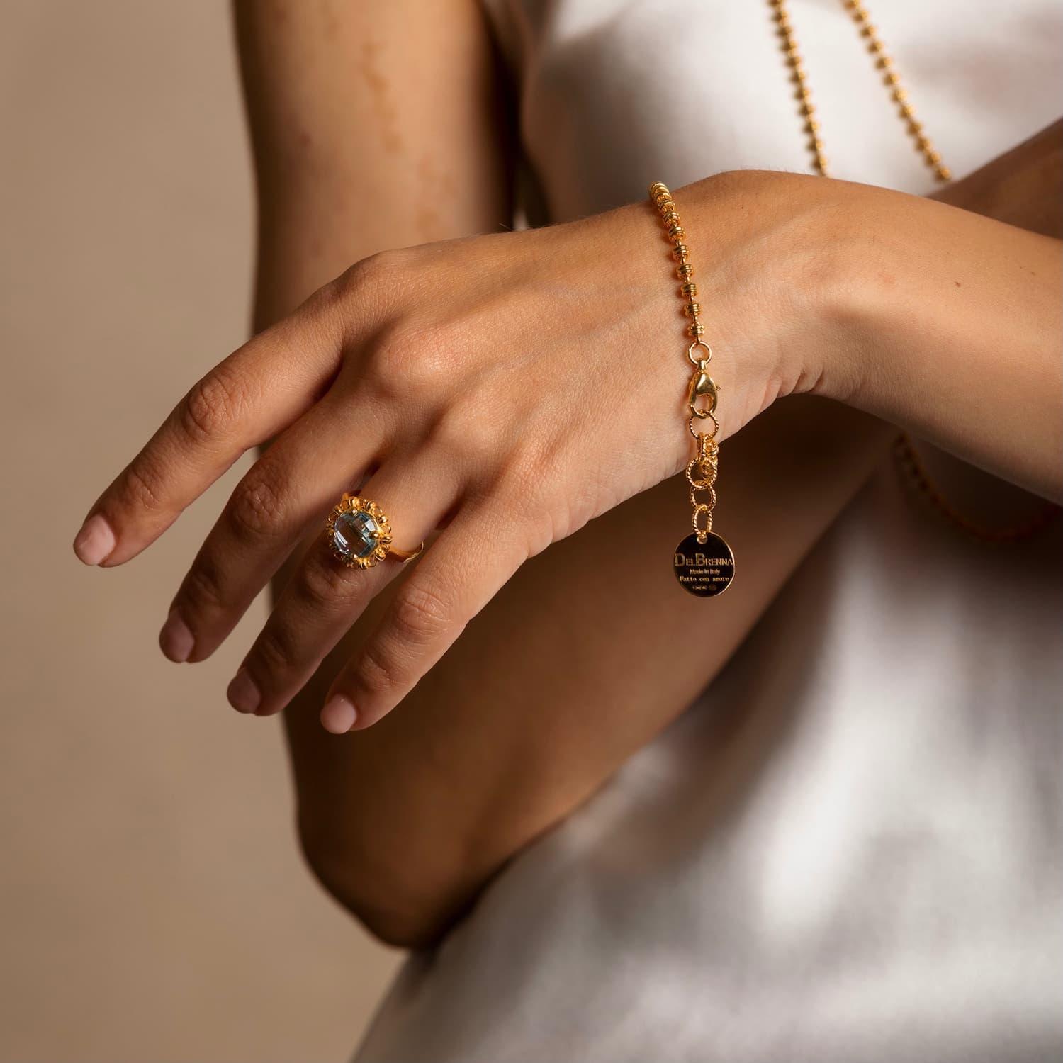 A closeup of a model wearing a delicate gold chain bracelet with a small circular gold charm and lobster clasp all in 24K yellow gold finish over 925% sterling silver. The gold bracelet is designed from the iconic DelBrenna Links collection - Italian jewelry designs hand-crafted in Tuscany. 