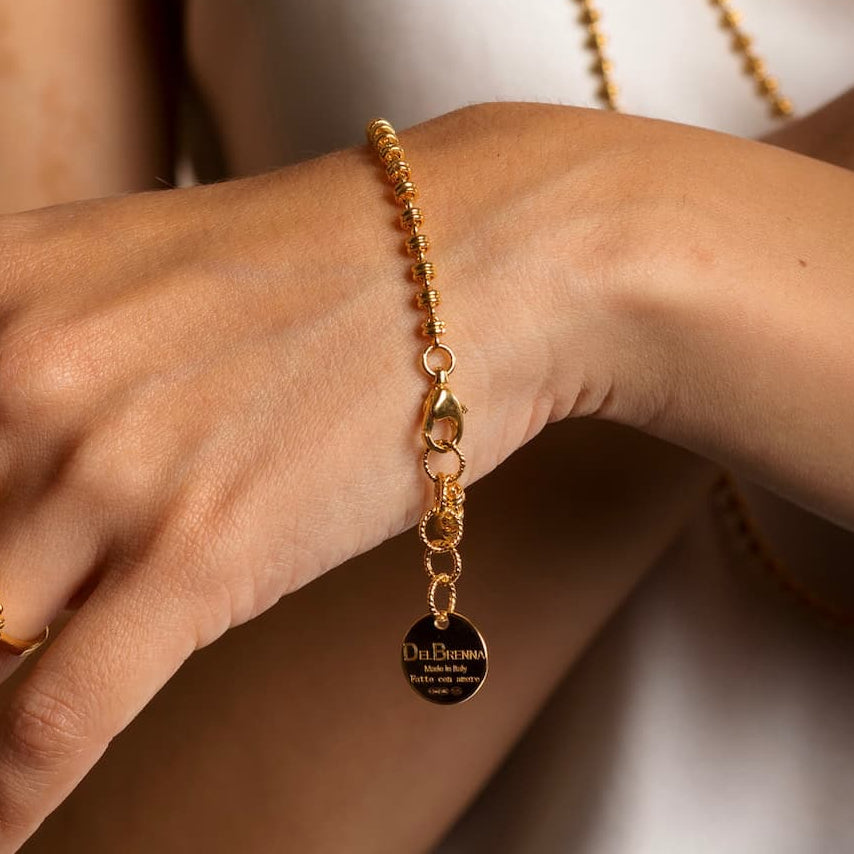 A closeup of a model wearing a delicate gold chain bracelet with a small circular gold charm and lobster clasp all in 24K yellow gold finish over 925% sterling silver. The gold bracelet is designed from the iconic DelBrenna Links collection - Italian jewelry designs hand-crafted in Tuscany.