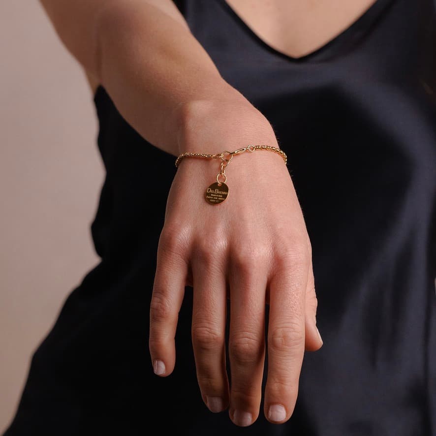 A model holding their hand out shows a delicate gold chain bracelet with a small circular gold charm and lobster clasp all in 24K yellow gold finish over 925% sterling silver. The gold bracelet is designed from the iconic DelBrenna Links collection - Italian jewelry designs hand-crafted in Tuscany.