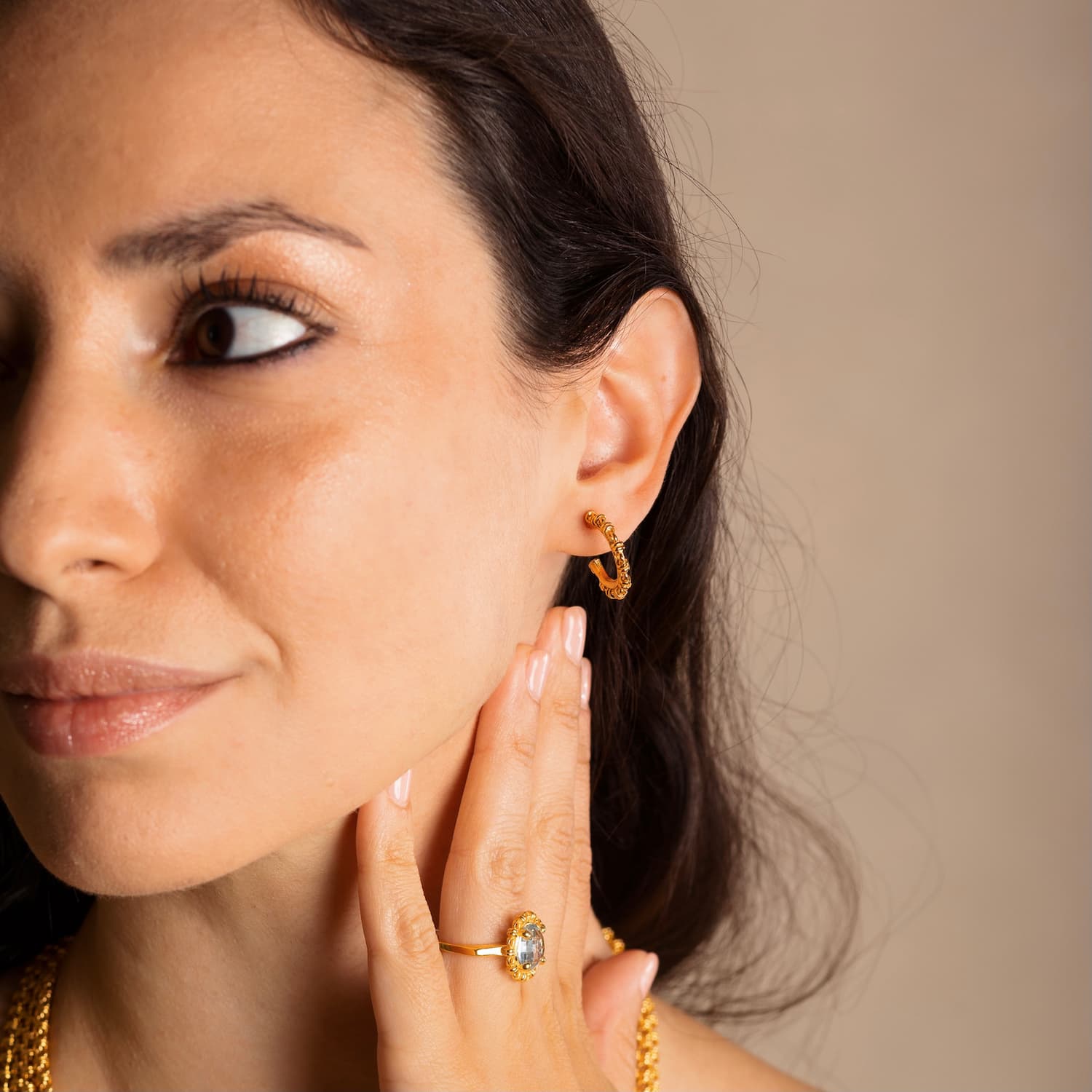 A model wearing four gold chains with matching gold hoop earrings and a gold ring in the same iconic chain design around a semi-precious gemstone. All hand-crafted Italian jewelry is made by DelBrenna Italian Jewelers in Tuscany. 