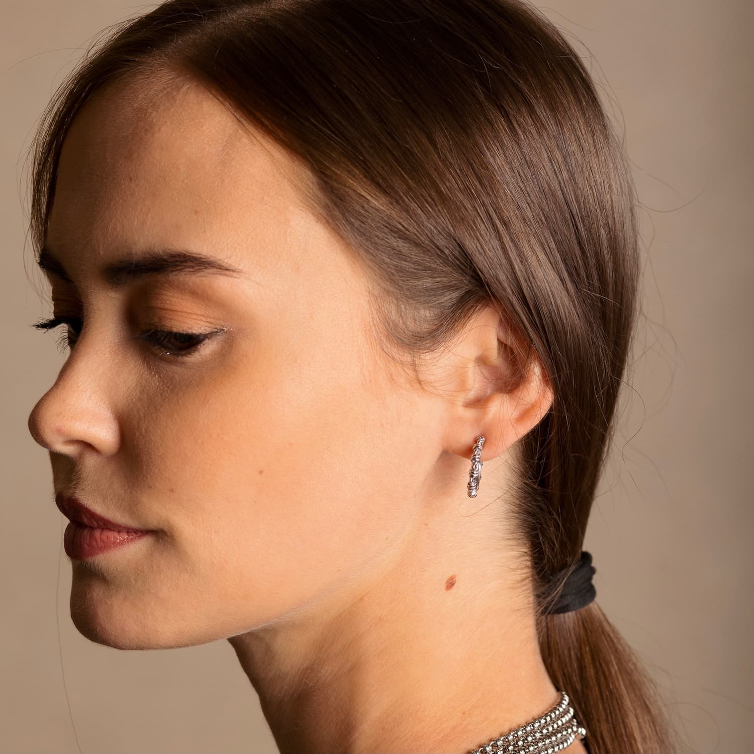 A model with dark hair wearing silver hoop earrings designed and hand-crafted by DelBrenna Italian Jewelers in Tuscany. The earrings and necklace shown here are designed based on the iconic Links collection of DelBrenna silver chains, necklaces, rings, and bracelets.