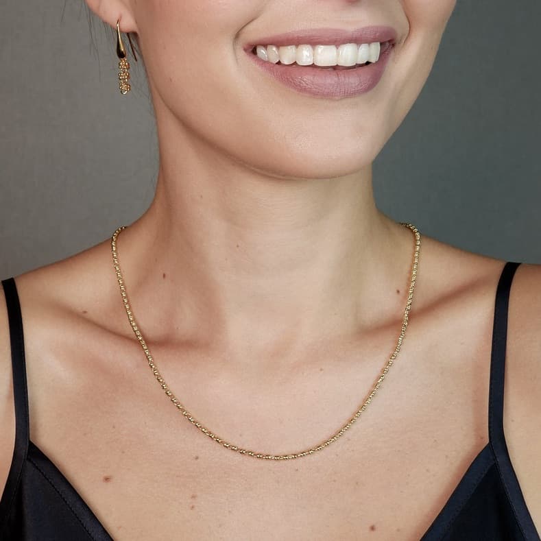A front-facing, closeup view of a model wearing a short (18-inch) gold necklace with matching gold earrings. The necklace and earrings are a delicate 2MM version of the iconic gold chain designed by DelBrenna Italian jewelry designers in 1974 in Tuscany.