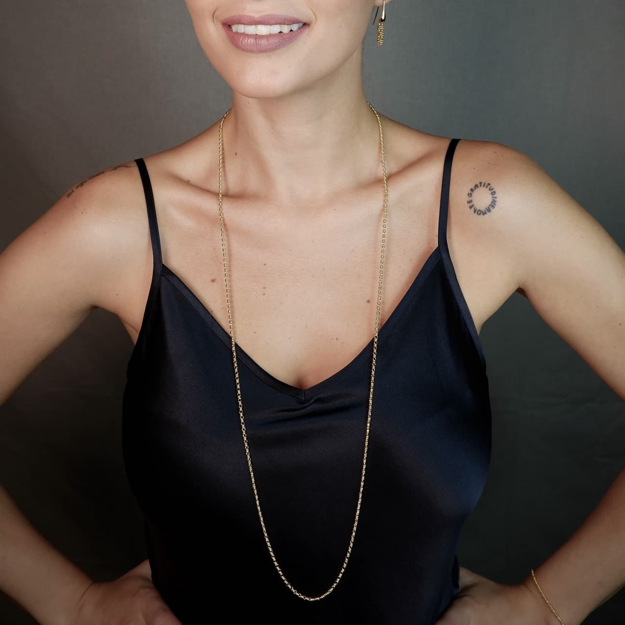 A front-facing, closeup view of a model wearing a long (22-inch) gold necklace with matching gold earrings. The necklace and earrings are a delicate 2MM version of the iconic gold chain designed by DelBrenna Italian jewelry designers in 1974 in Tuscany.