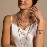 A model wearing four silver chains in varying lengths from a short, 16-inch silver chain to a 36-inch silver chain with matching silver earrings and a silver ring in the same iconic chain design around a semi-precious gemstone. All hand-crafted Italian jewelry is made by DelBrenna Italian Jewelers in Tuscany.