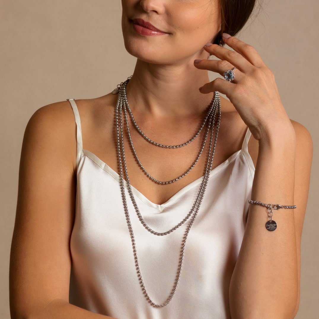 A model wearing four silver chains in varying lengths from a short, 16-inch silver chain to a 36-inch silver chain with matching silver earrings and a silver ring in the same iconic chain design around a semi-precious gemstone. All hand-crafted Italian jewelry is made by DelBrenna Italian Jewelers in Tuscany. 