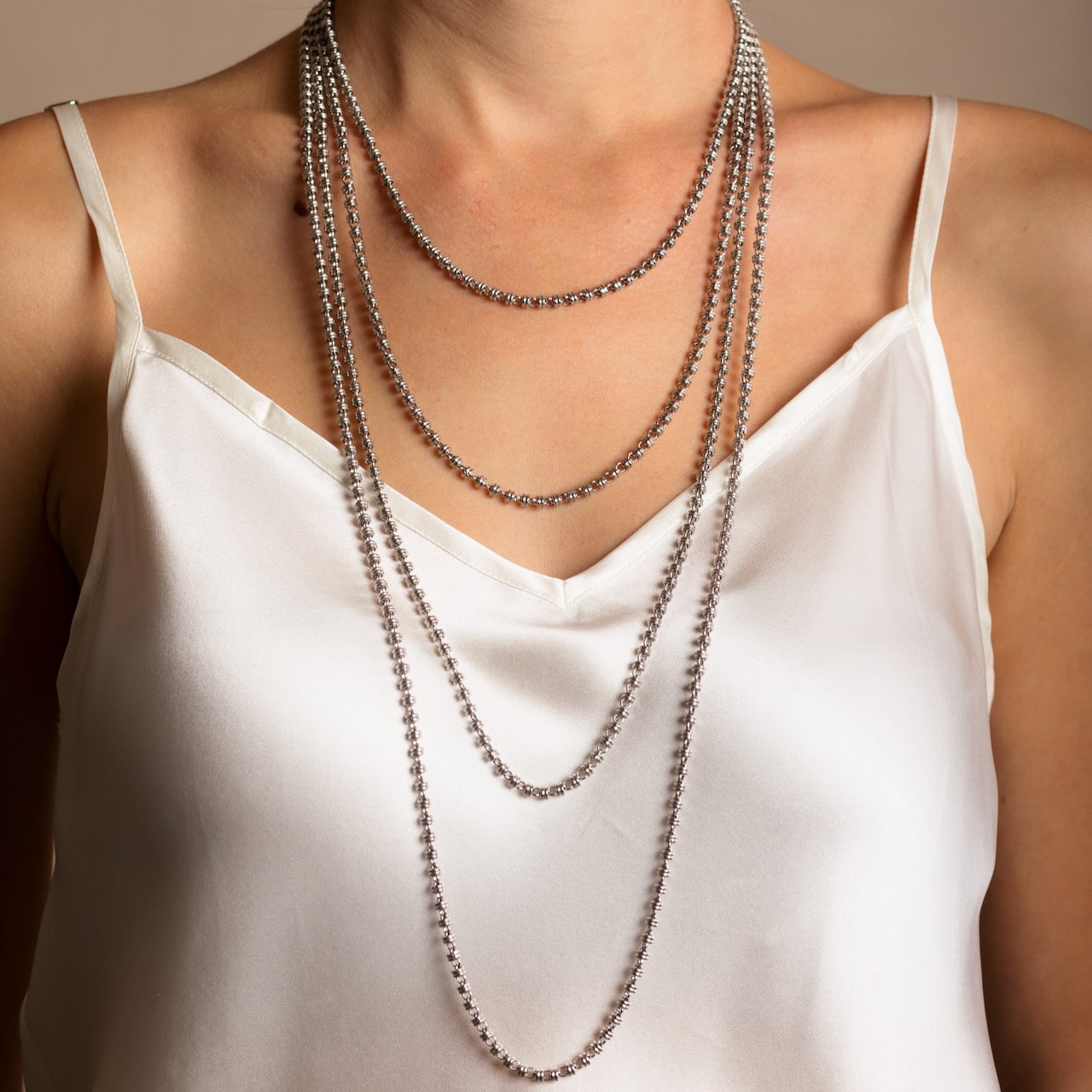 A model wearing four silver chains in varying lengths from a short, 16-inch silver chain to a 36-inch silver chain. These hand-crafted Italian silver chains are made by DelBrenna Italian Jewelers in Tuscany.