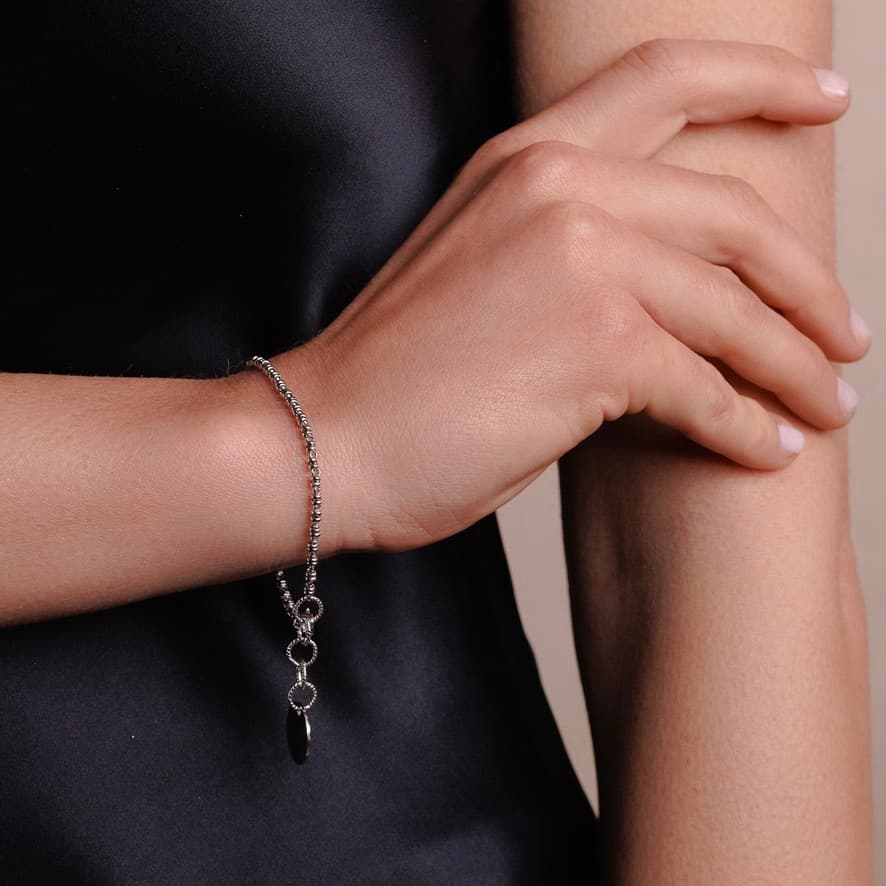 A closeup of a model wearing a delicate silver chain bracelet with a small circular silver charm and lobster clasp all in Rhodium finish over 925% sterling silver. The silver bracelet is designed from the iconic DelBrenna Links collection - Italian jewelry designs hand-crafted in Tuscany.