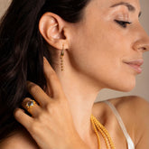 A model holding her hair back to show four gold chains with matching long gold chain earrings and a gold ring in the same iconic chain design around a semi-precious gemstone. All hand-crafted Italian jewelry is made by DelBrenna Italian Jewelers in Tuscany.