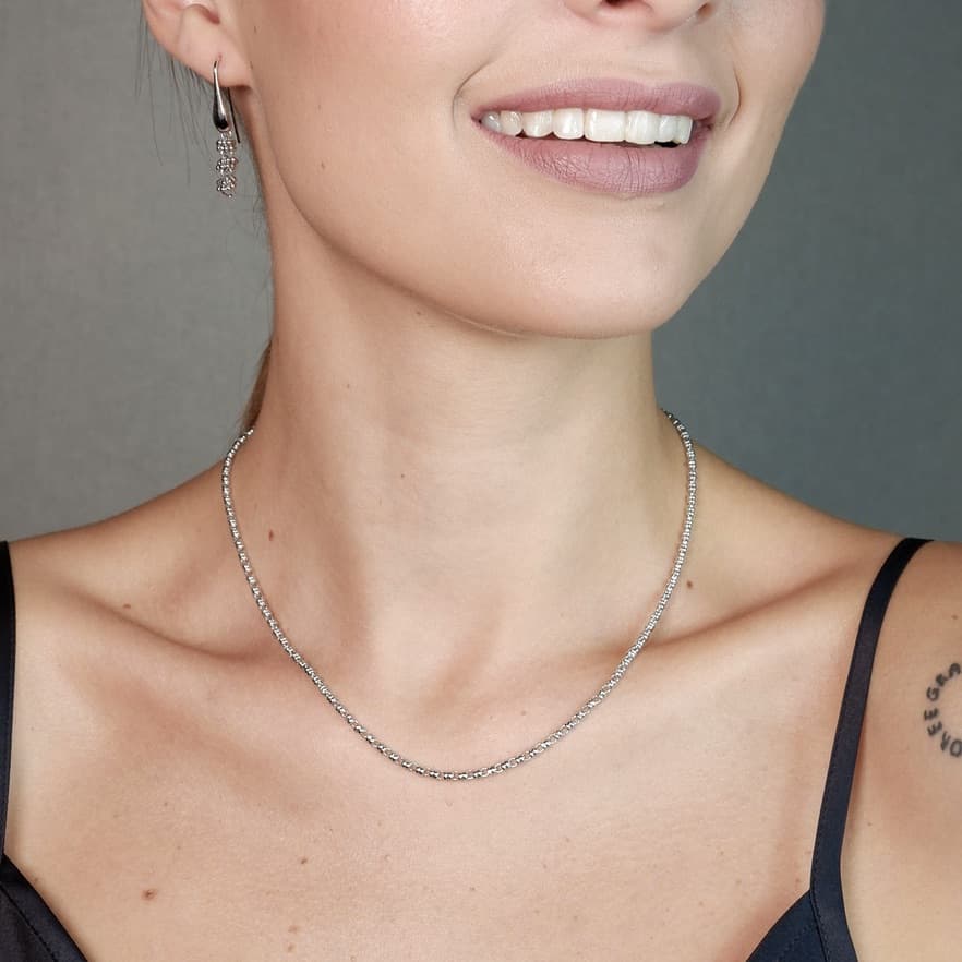 A front-facing, closeup view of a model wearing a short (16-inch) silver necklace with matching silver earrings. The necklace and earrings are a delicate 2MM version of the iconic silver chain designed by DelBrenna Italian jewelry designers in 1974 in Tuscany.