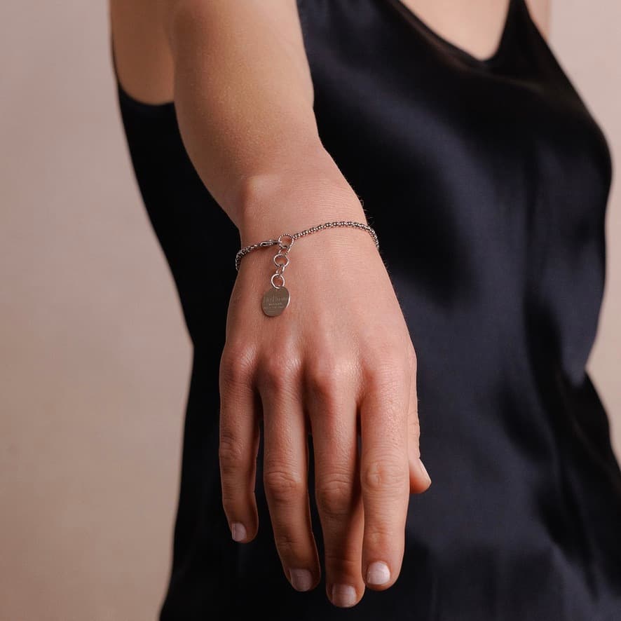 A model holding their hand out shows a delicate silver chain bracelet with a small circular silver charm and lobster clasp all in Rhodium finish over 925% sterling silver. The silver bracelet is designed from the iconic DelBrenna Links collection - Italian jewelry designs hand-crafted in Tuscany.