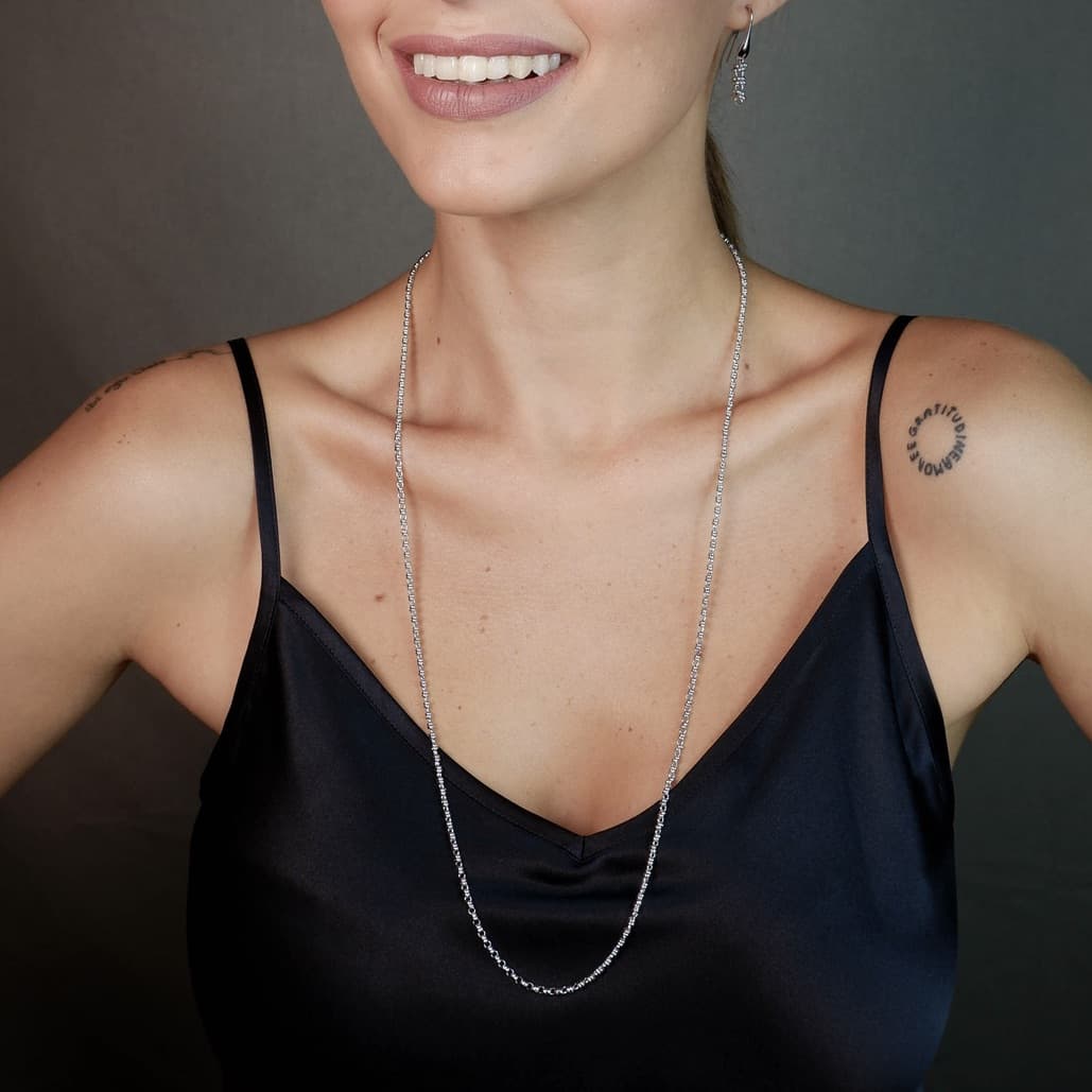A front-facing, closeup view of a model wearing a long (30-inch) silver necklace with matching silver earrings. The necklace and earrings are a delicate 2MM version of the iconic silver chain designed by DelBrenna Italian jewelry designers in 1974 in Tuscany.