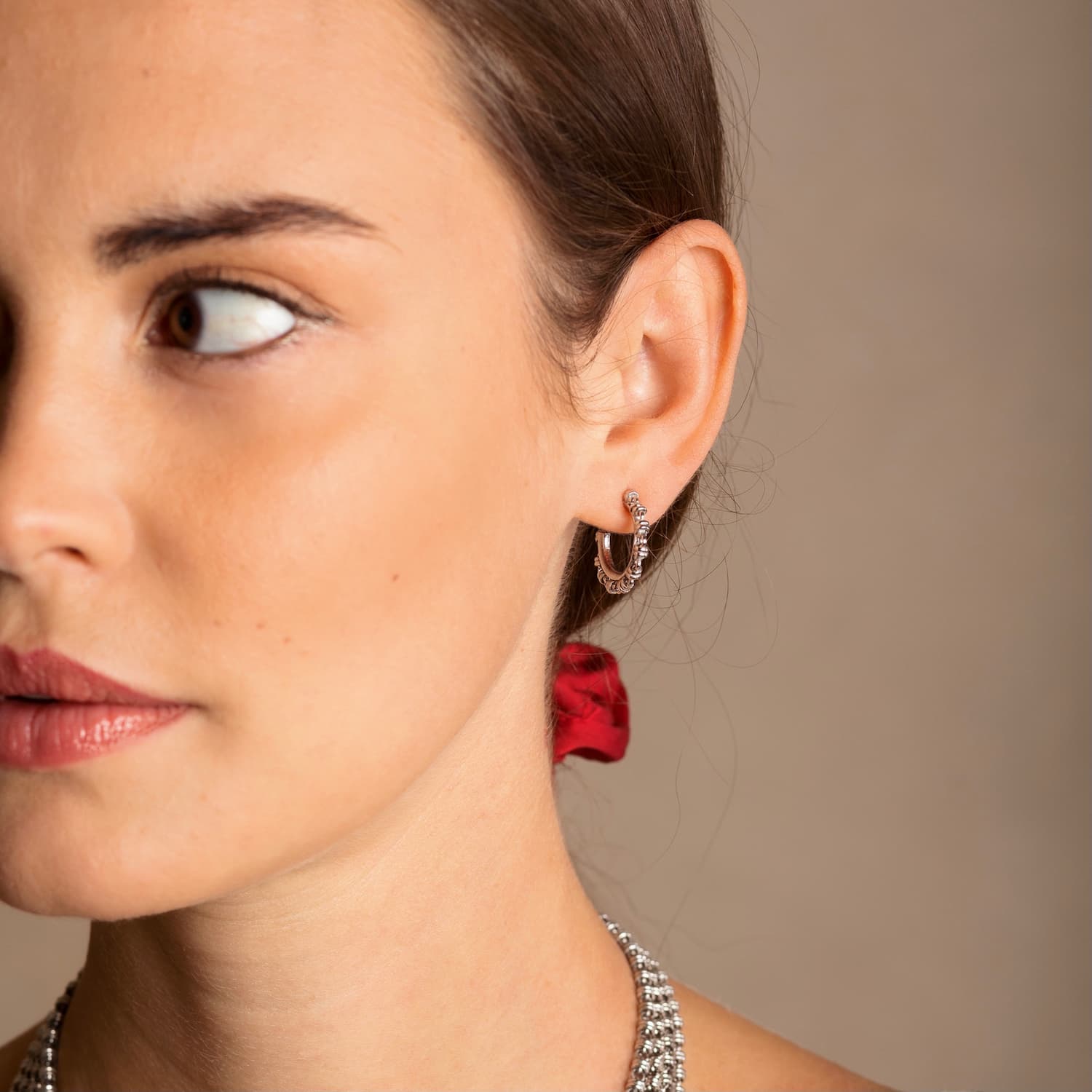 A closeup of a model wearing silver hoop earrings designed and hand-crafted by DelBrenna Italian Jewelers in Tuscany. The earrings and necklace shown here are designed based on the iconic Links collection of DelBrenna silver chains, necklaces, rings, and bracelets.