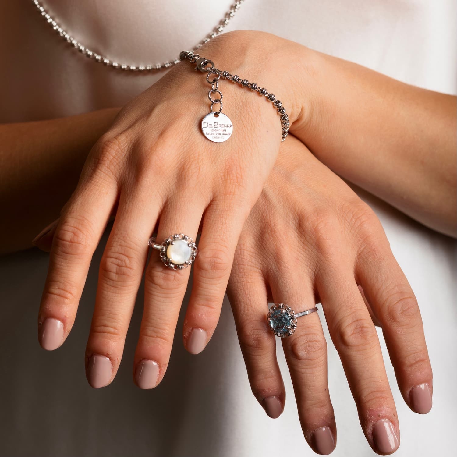 A closeup of a model’s hands crosses to show two silver rings with semi-precious gemstones set inside a silver chain design that matches the silver bracelet and the silver necklace. All jewelry is hand-crafted by DelBrenna Italian Jewelry designers in Tuscany. 