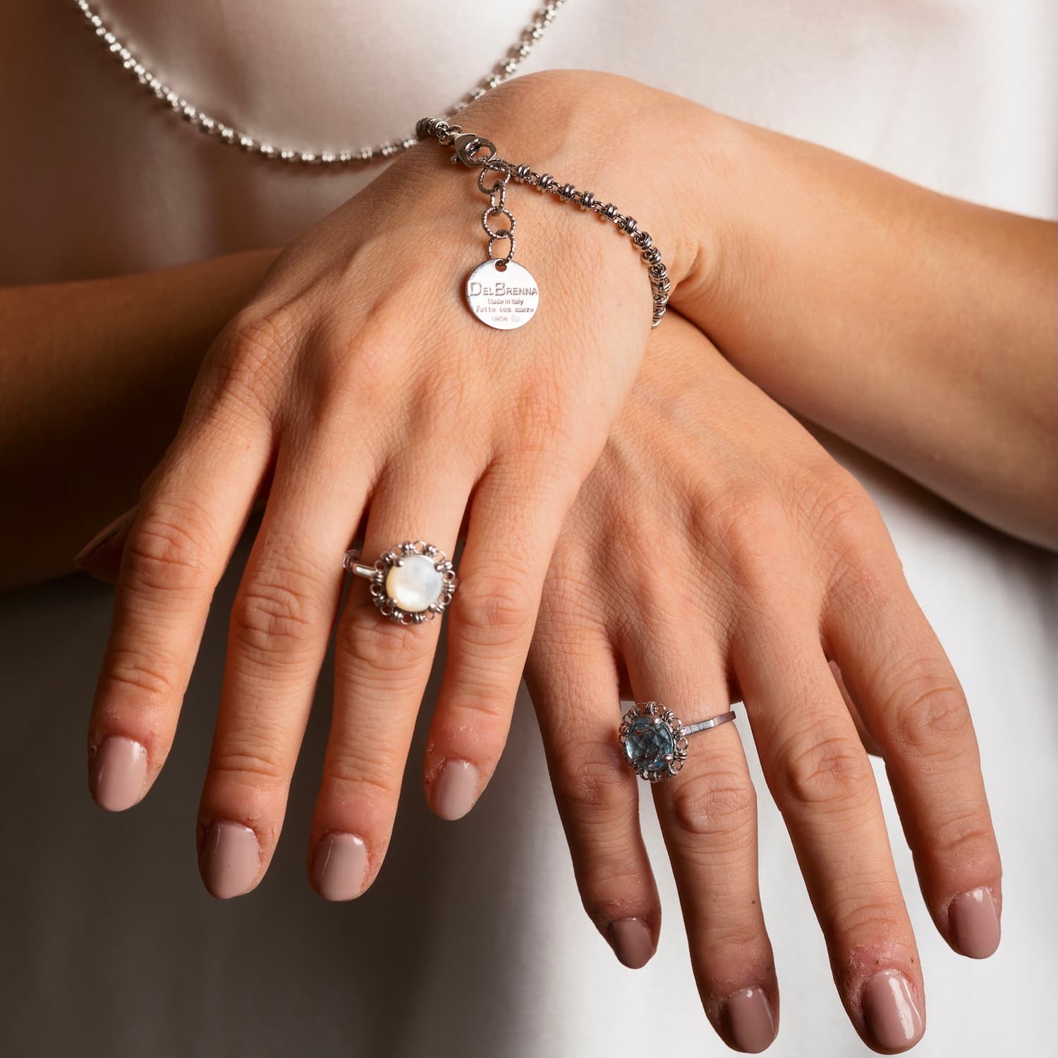 A closeup of a model’s hands crosses to show two silver rings with semi-precious gemstones set inside a silver chain design that matches the silver bracelet and the silver necklace. All jewelry is hand-crafted by DelBrenna Italian Jewelry designers in Tuscany.