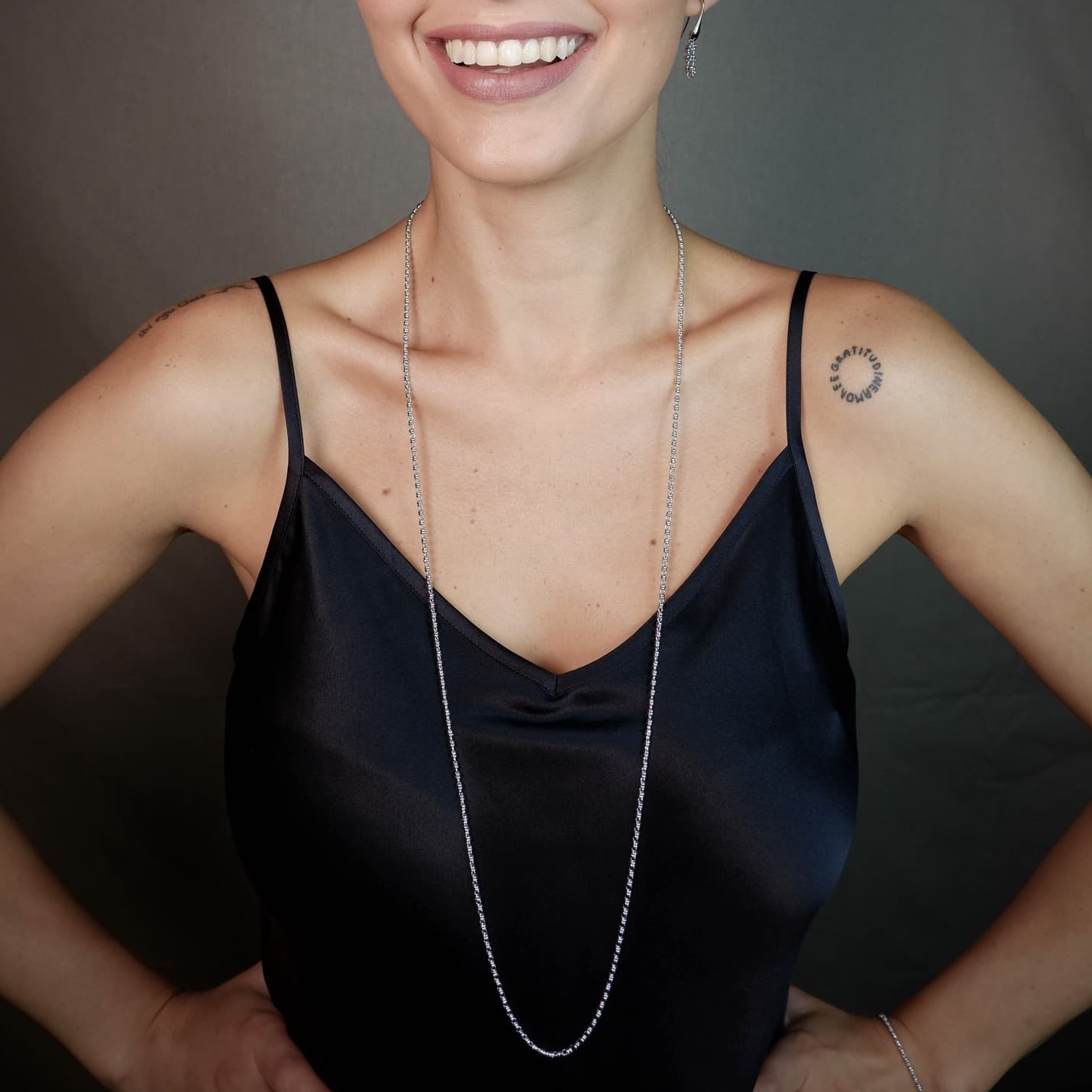 A front-facing, closeup view of a model wearing a long (34-inch) silver necklace with matching silver earrings. The necklace and earrings are a delicate 2MM version of the iconic silver chain designed by DelBrenna Italian jewelry designers in 1974 in Tuscany.
