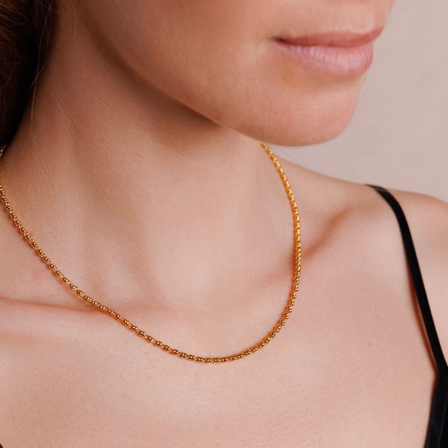 A left-facing, close-up view of a model wearing a short (16-inch) gold necklace. The necklace is a delicate 2MM version of the iconic gold chain designed by DelBrenna Italian jewelry designers in 1974 in Tuscany.