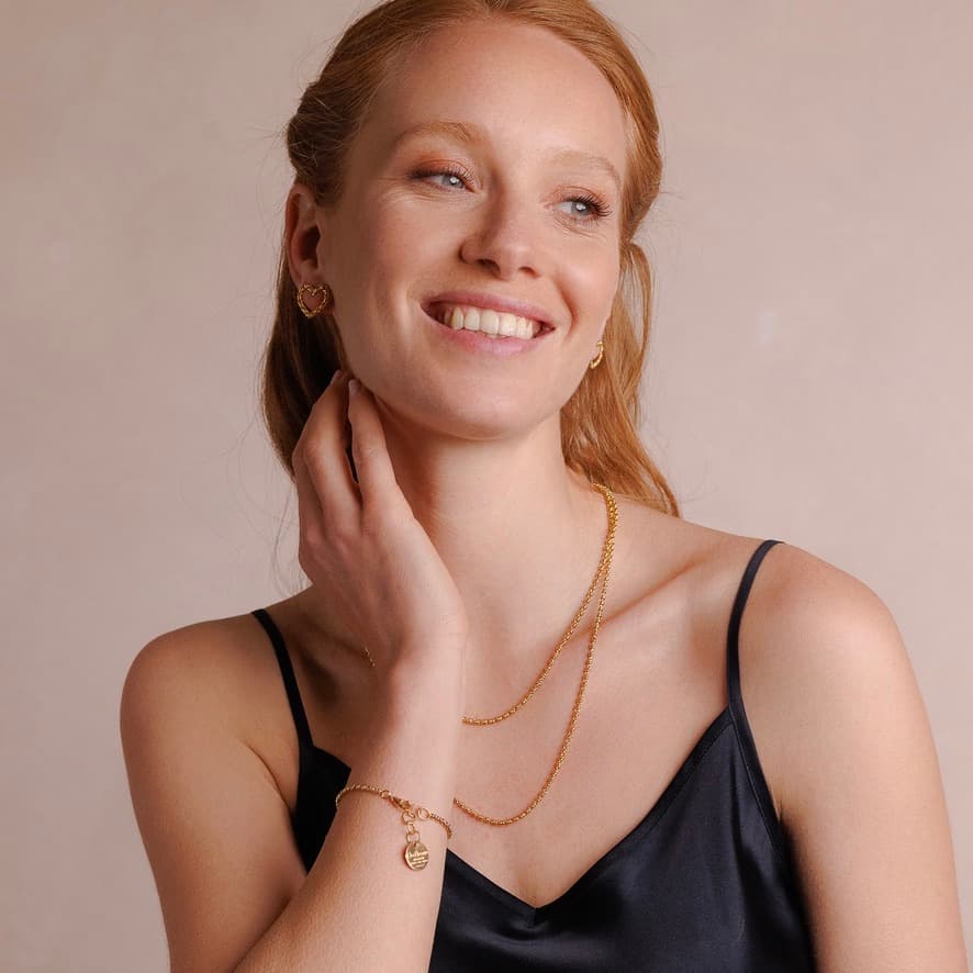 A model wearing two delicate, hand-crafted 2MM gold chains in two different lengths: a short, 16-18” gold chain necklace and a 20-22” gold necklace with matching gold heart earrings and a gold bracelet with a gold charm. All jewelry is hand-crafted by DelBrenna Italian Jewelry designers in Tuscany.
