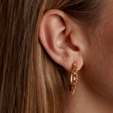 A closeup of a model wearing large gold hoop earrings with a chain design from DelBrenna Italian jewelry design. The earrings are hand-crafted in Tuscany.