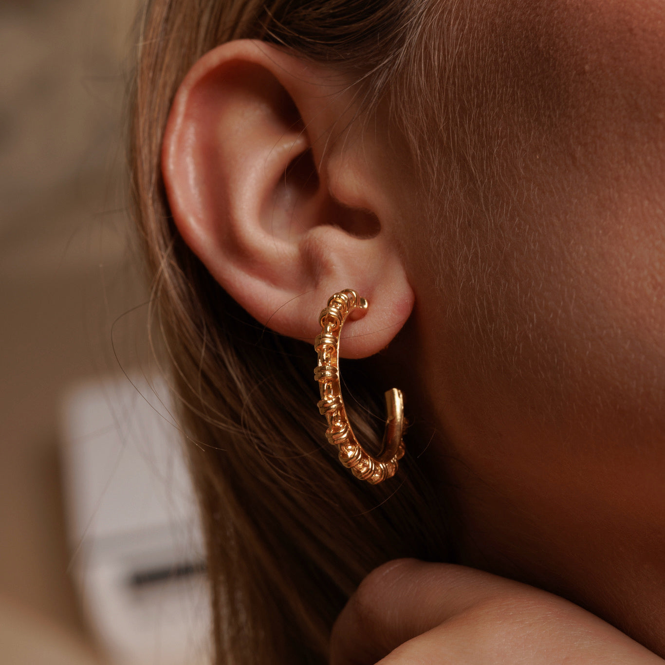 A closeup, side view of a model wearing large gold hoop earrings with a chain design from DelBrenna Italian jewelry design. The earrings are hand-crafted in Tuscany.