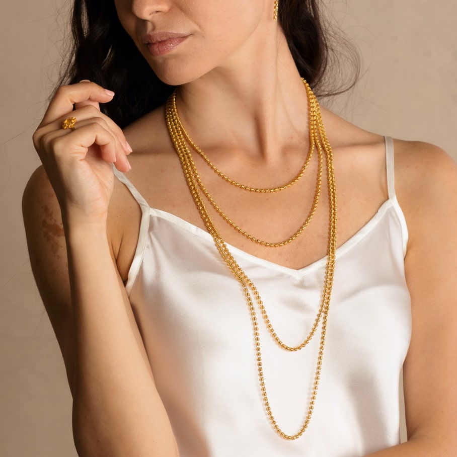 A model wearing four gold chains in varying lengths from a short, 16-inch gold chain to a 36-inch gold chain with matching gold earrings and a gold ring in the same iconic chain design around a semi-precious gemstone. All hand-crafted Italian jewelry is made by DelBrenna Italian Jewelers in Tuscany. 