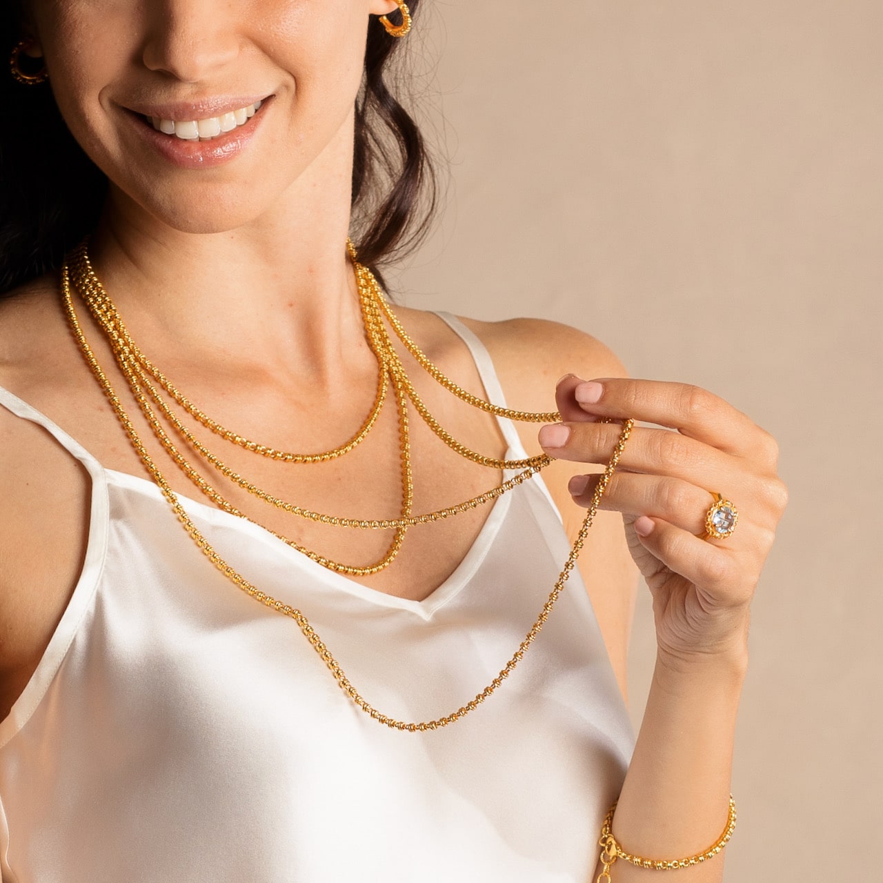 A model displaying four gold chains in varying lengths from a short, 16-inch gold chain to a 36-inch gold chain with matching gold earrings and a gold ring in the same iconic chain design around a semi-precious gemstone. All hand-crafted Italian jewelry is made by DelBrenna Italian Jewelers in Tuscany. 