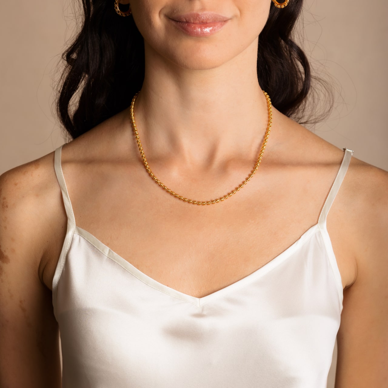 A model wearing a short (16-inch) DelBrenna Iconic Links 3MM gold necklace with matching Links 3MM large gold hoop earrings. Both pieces of hand-crafted Italian jewelry are made by DelBrenna Italian Jewelers in Tuscany. 
