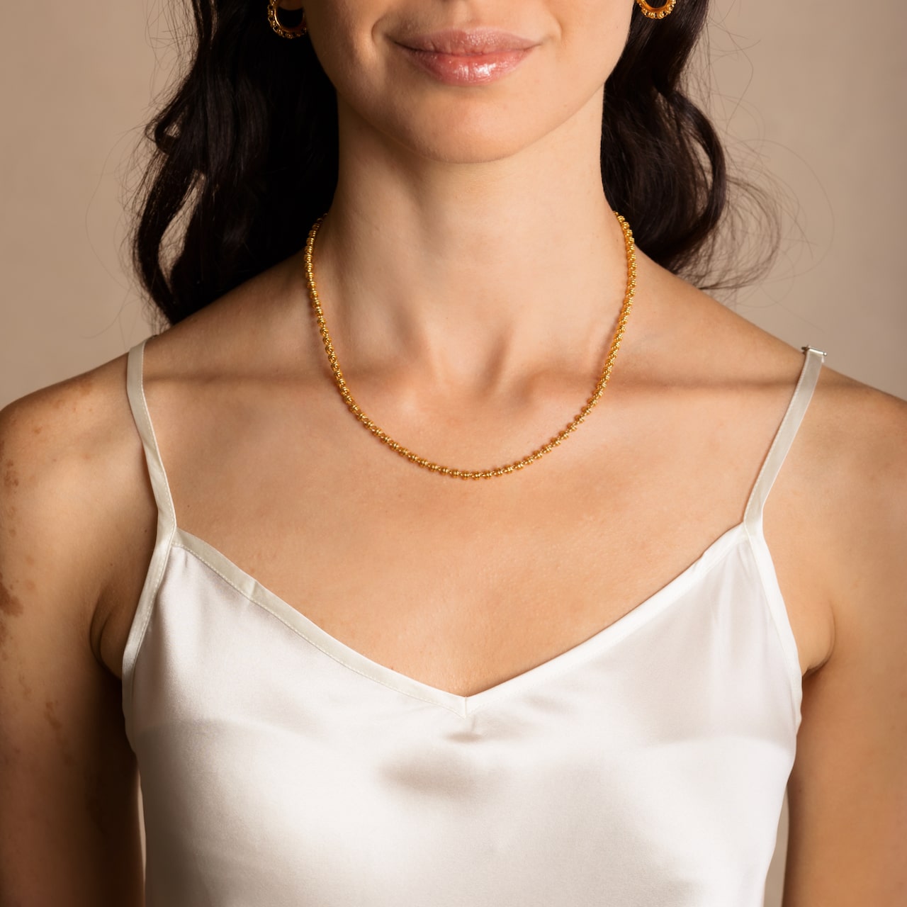 A model wearing a short (16-inch) DelBrenna Iconic Links 3MM gold necklace with matching Links 3MM large gold hoop earrings. Both pieces of hand-crafted Italian jewelry are made by DelBrenna Italian Jewelers in Tuscany.