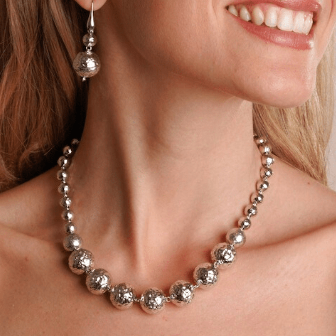 A model wearing a stunning sterling silver hammered bead necklace with beads of various sizes with matching sterling silver drop earrings - all handcrafted by artisans at DelBrenna Fine Jewelry of Cortana, Italy. 
