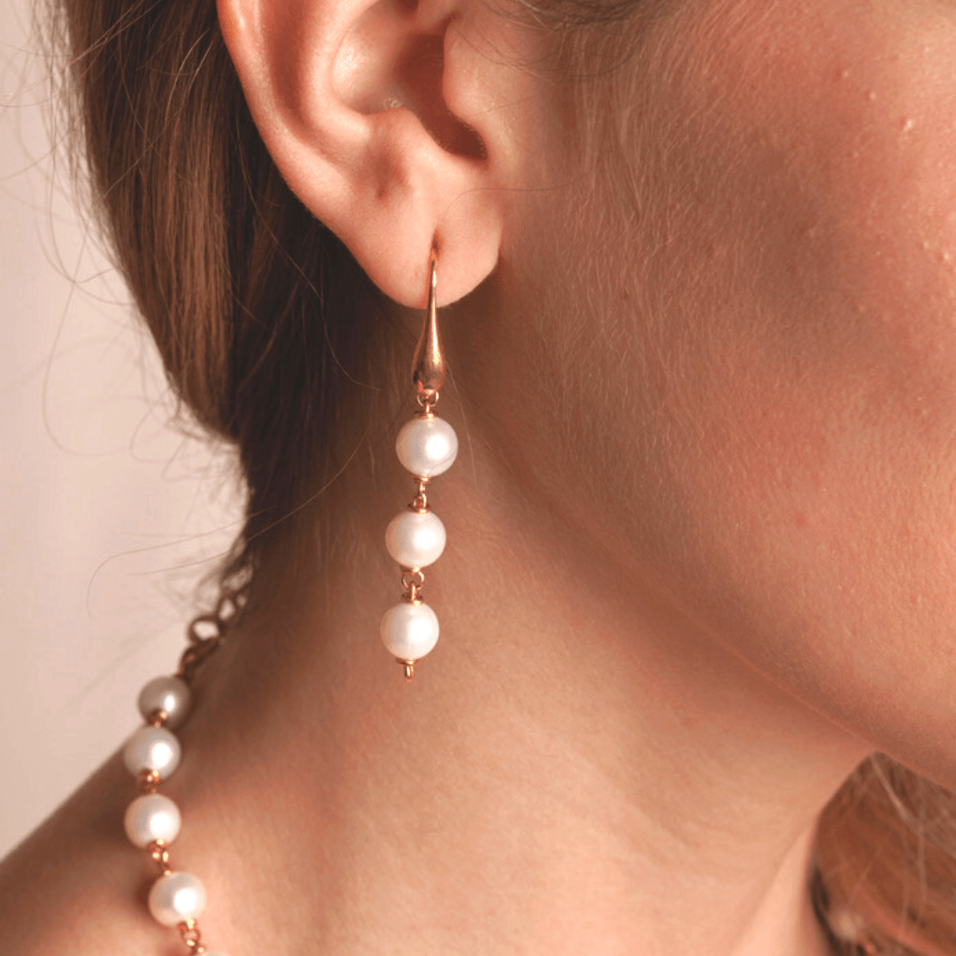 A model wearing DelBrenna's unique baroque pearl drop earrings in 925 silver with DelBrenna's Featured Bright Gold Finish. Earrings measure 2” (55mm). Pearls are 8mm in diameter with a hook closure. The model wears a matching pearl necklace. 