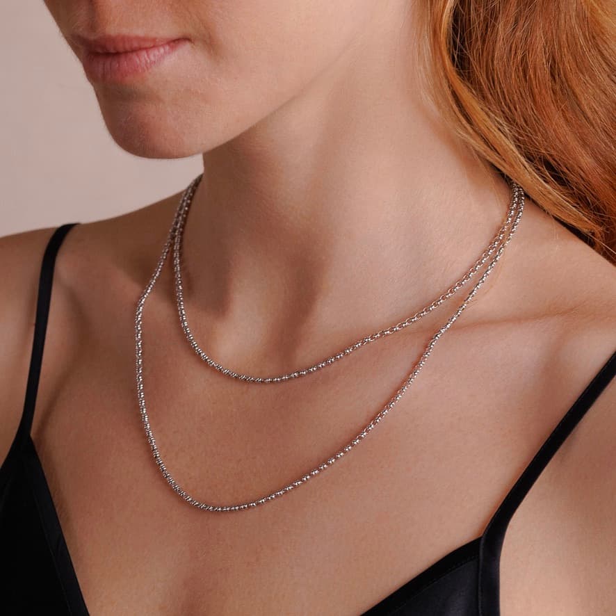 A right-side view of a model wearing two delicate, hand-crafted 2MM silver chains in two different lengths: a short, 16-18” silver chain necklace and a 20-22” silver necklace with matching silver heart earrings - all silver necklaces and earrings are crafted by DelBrenna Italian Jewelry designers in Tuscany.
