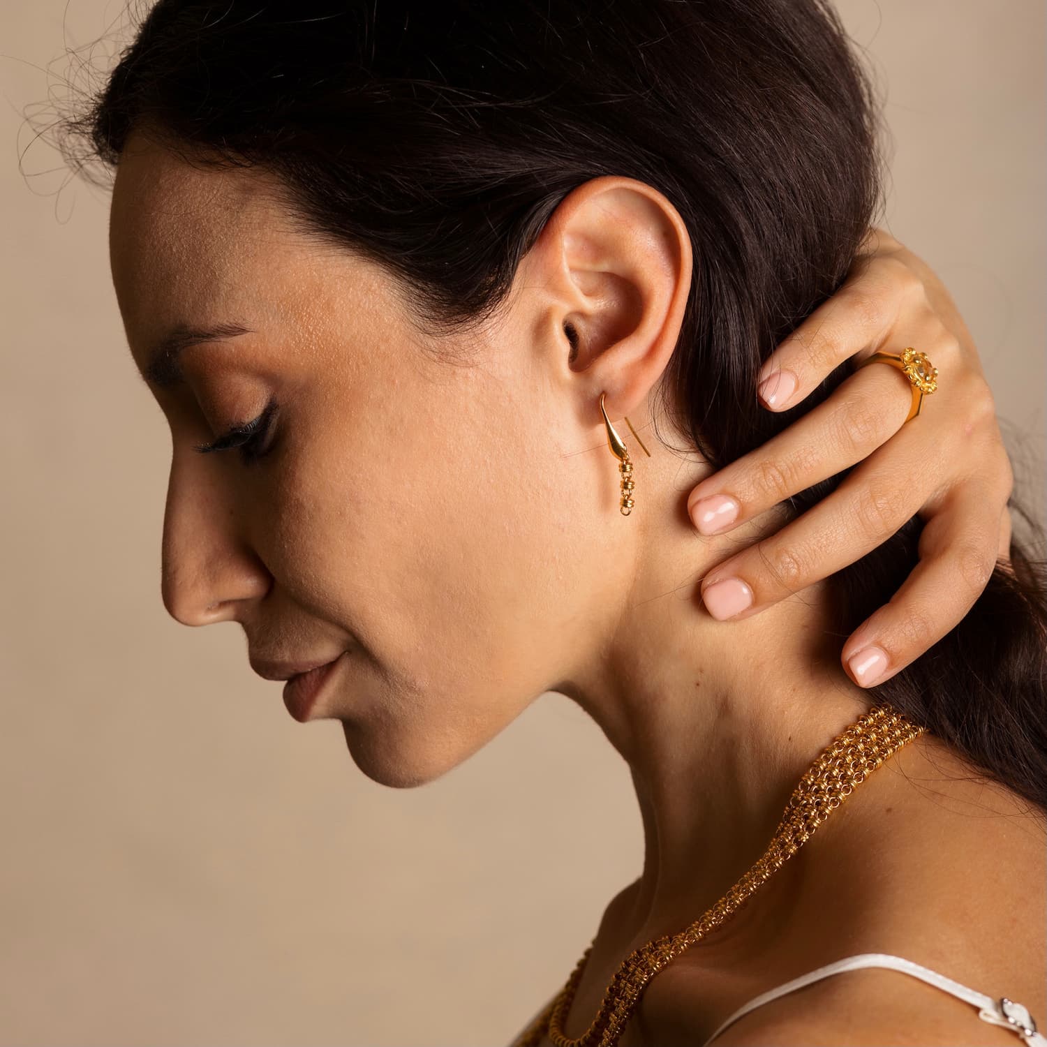 A model holding her hair back to show four gold chains with matching gold chain earrings and a gold ring in the same iconic chain design around a semi-precious gemstone. All hand-crafted Italian jewelry is made by DelBrenna Italian Jewelers in Tuscany. 