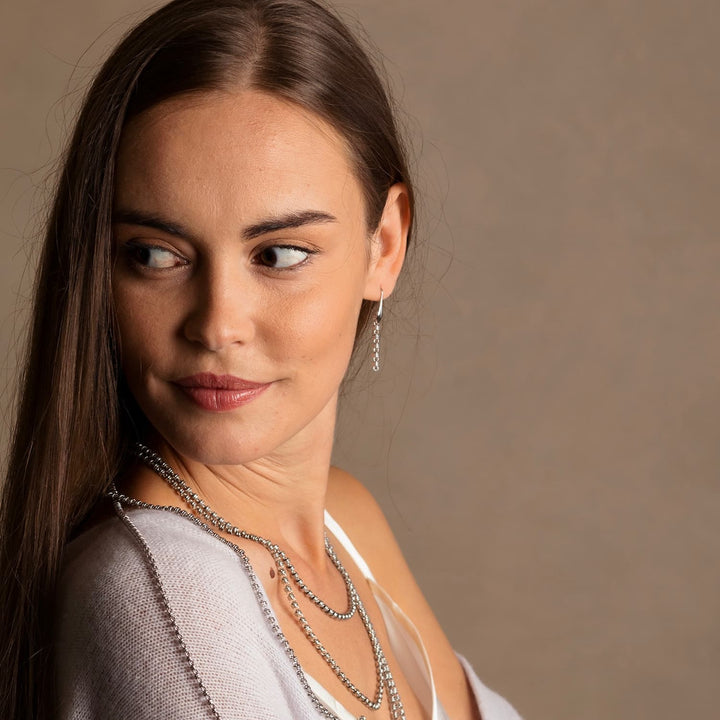 A model wearing long silver chain earrings and silver chain necklaces designed and hand-crafted by DelBrenna Italian Jewelers in Tuscany. The earrings are designed based on the iconic Links collection of DelBrenna silver chains, necklaces, rings, and bracelets.