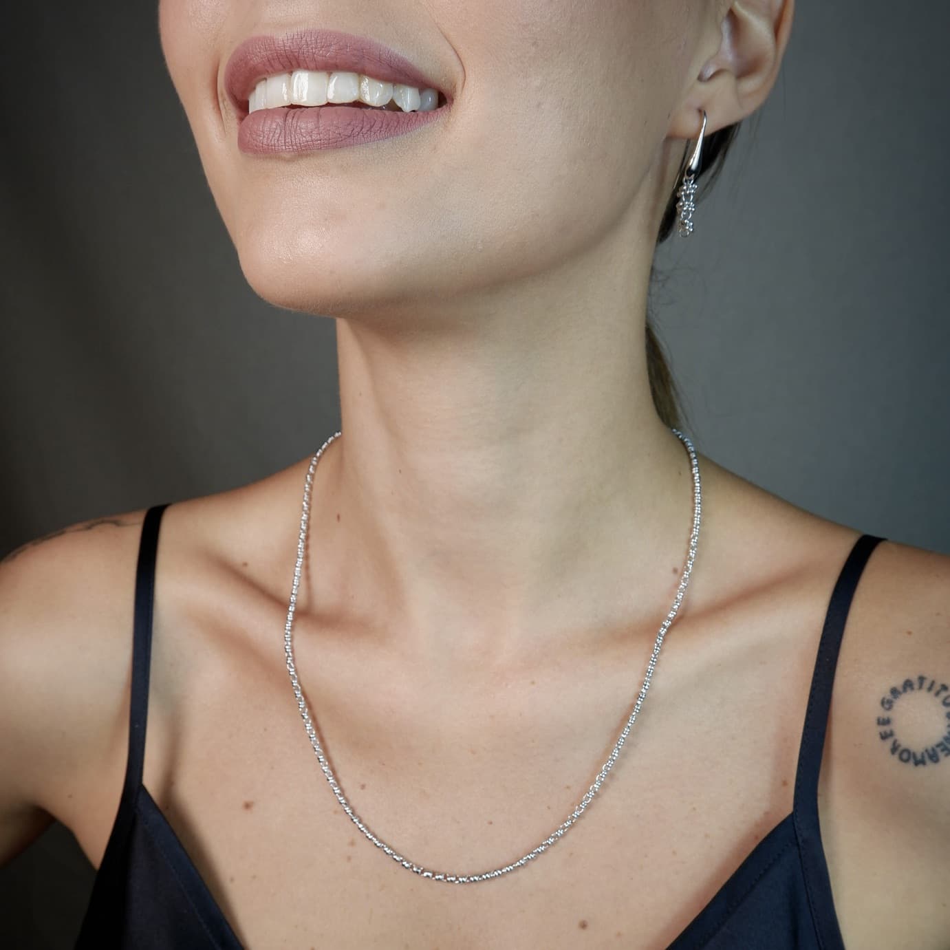 A front-facing, closeup view of a model wearing a short (18-inch) silver necklace with matching silver earrings. The necklace and earrings are a delicate 2MM version of the iconic silver chain designed by DelBrenna Italian jewelry designers in 1974 in Tuscany. 