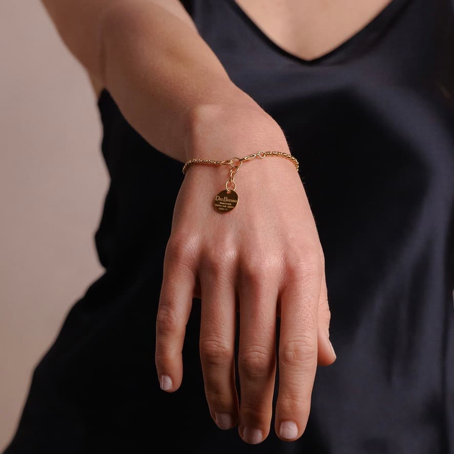 A model holding their hand out shows a delicate gold chain bracelet with a small circular gold charm and lobster clasp all in 24K yellow gold finish over 925% sterling silver. The gold bracelet is designed from the iconic DelBrenna Links collection - Italian jewelry designs hand-crafted in Tuscany. 