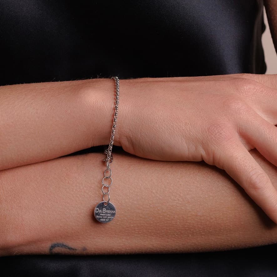 A model wearing a delicate silver chain bracelet with a small circular silver charm and lobster clasp all in Rhodium finish over 925% sterling silver. The silver bracelet is designed from the iconic DelBrenna Links collection - Italian jewelry designs hand-crafted in Tuscany. 