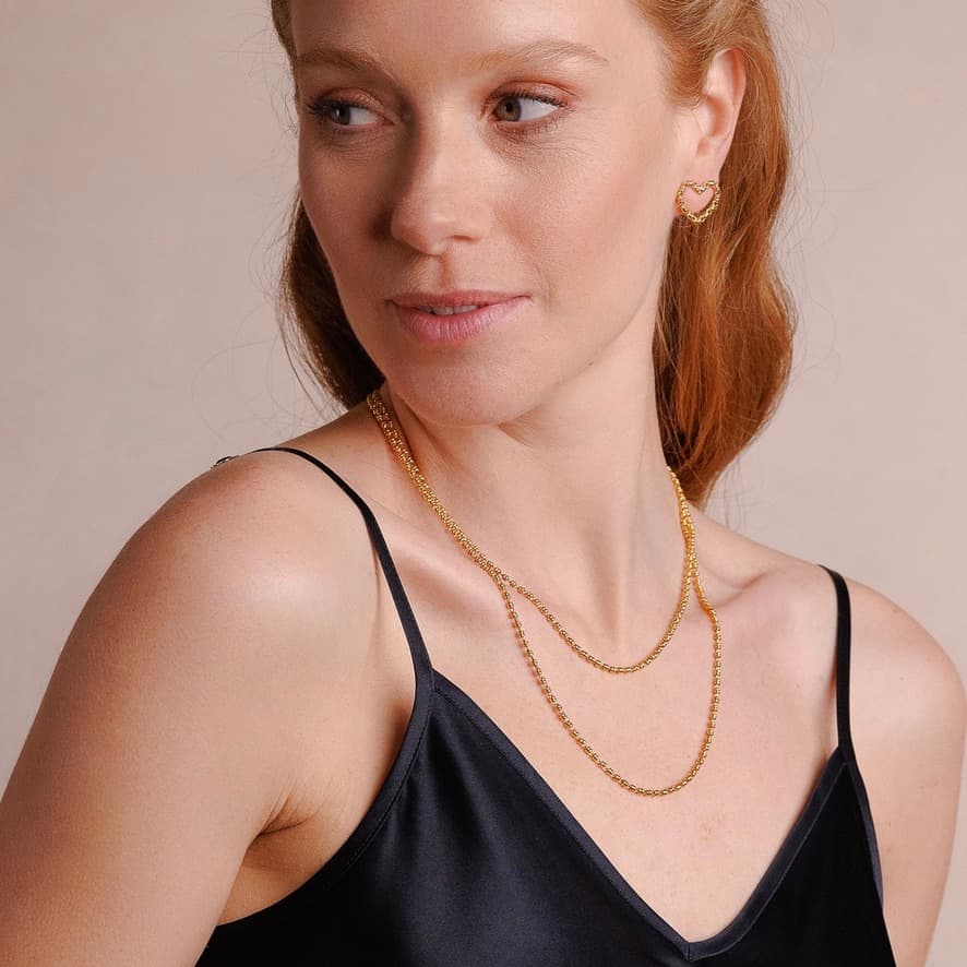 A model wearing two delicate, hand-crafted 2MM gold chains in two different lengths: a short, 16-18” gold chain necklace and a 20-22” gold necklace with matching gold heart earrings - all gold necklaces and earrings are crafted by DelBrenna Italian Jewelry designers in Tuscany.  