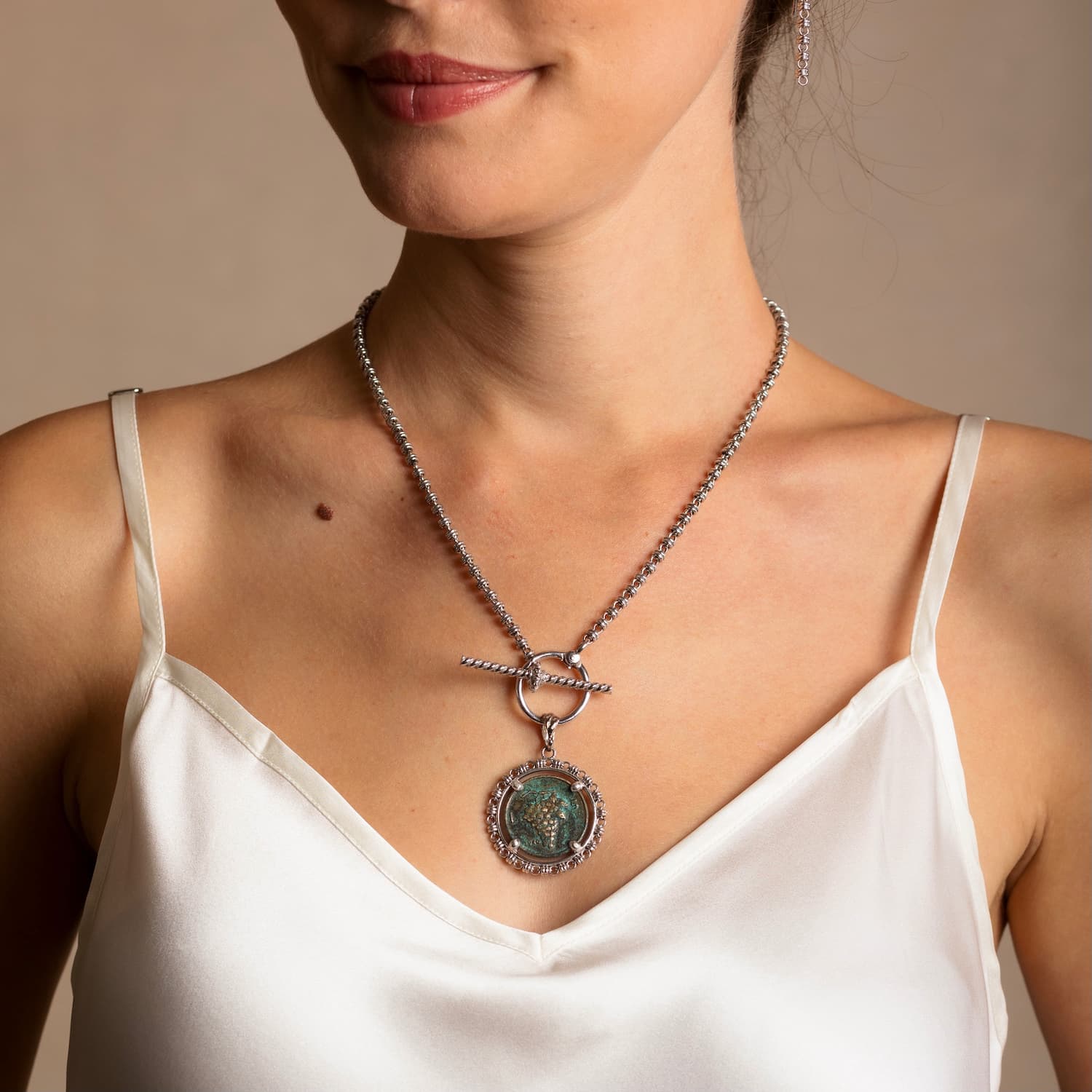 A model wearing a silver necklace with a toggle clasp, a coin pendant, and silver earrings to match the silver chain in the necklace - both from the Links 3mm collection from DelBrenna Italian Jewelry designers and artisans. Hand-crafted in Tuscany.