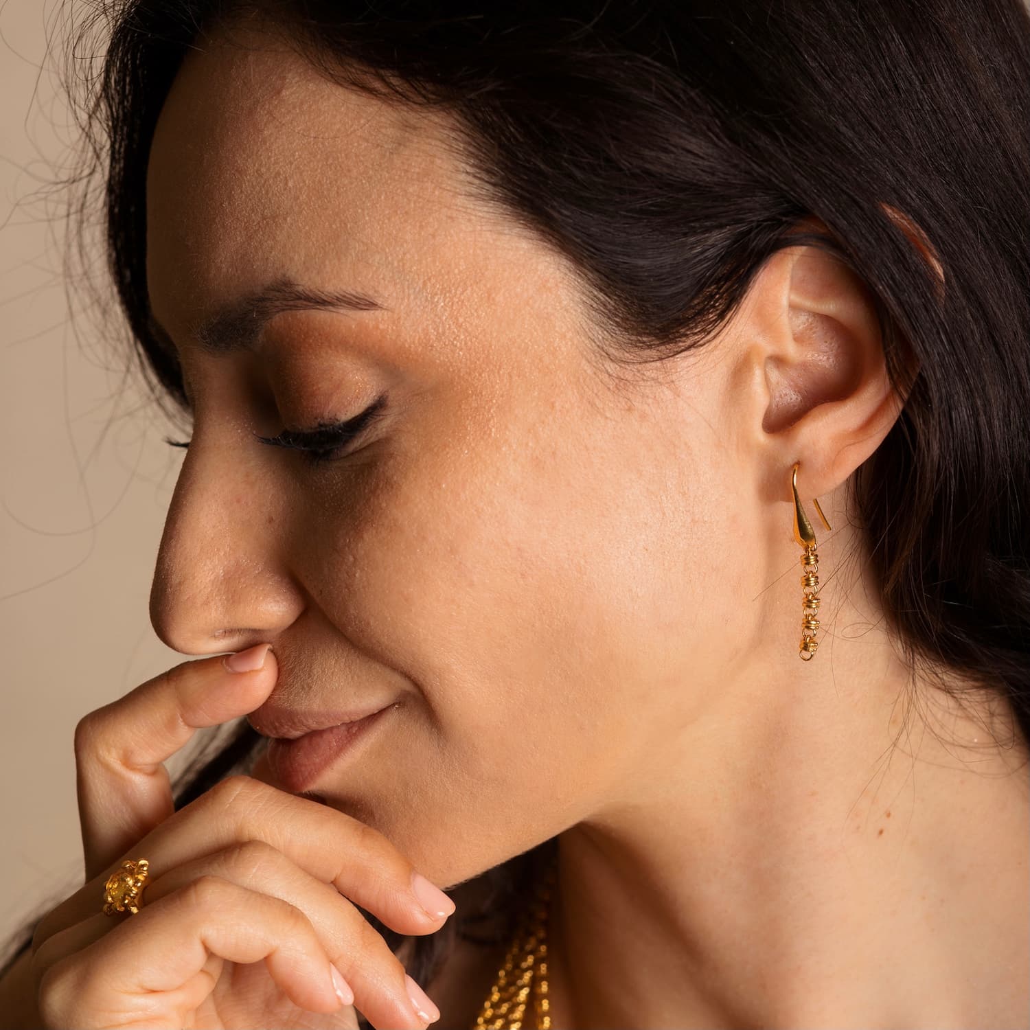 A model wearing four gold chains with matching long gold chain earrings in the same iconic chain design around a semi-precious gemstone. All hand-crafted Italian jewelry is made by DelBrenna Italian Jewelers in Tuscany. 