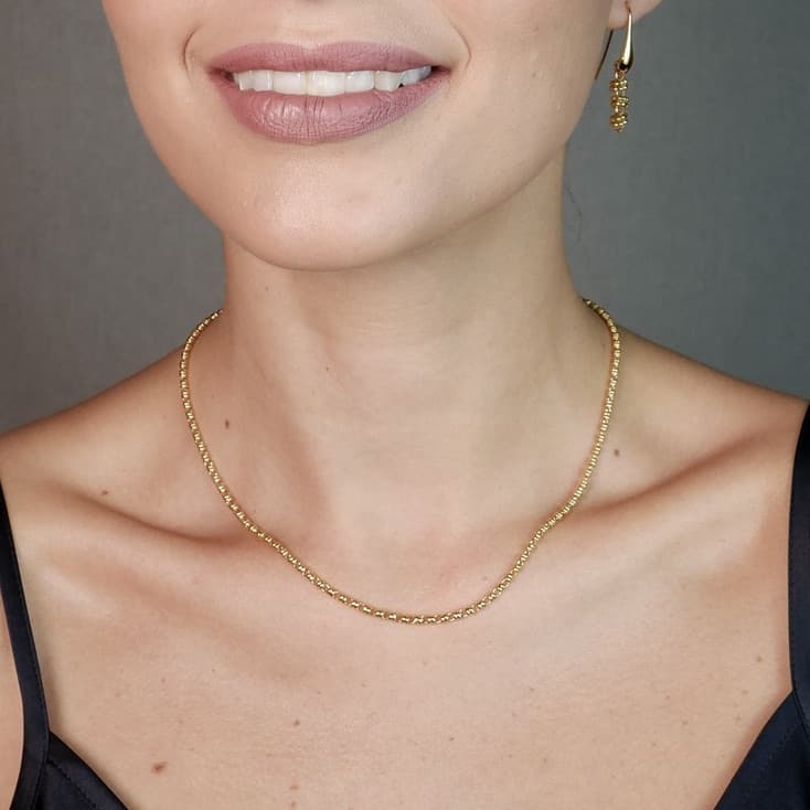 A front-facing, closeup view of a model wearing a short (16-inch) gold necklace with matching gold earrings. The necklace and earrings are a delicate 2MM version of the iconic gold chain designed by DelBrenna Italian jewelry designers in 1974 in Tuscany. 