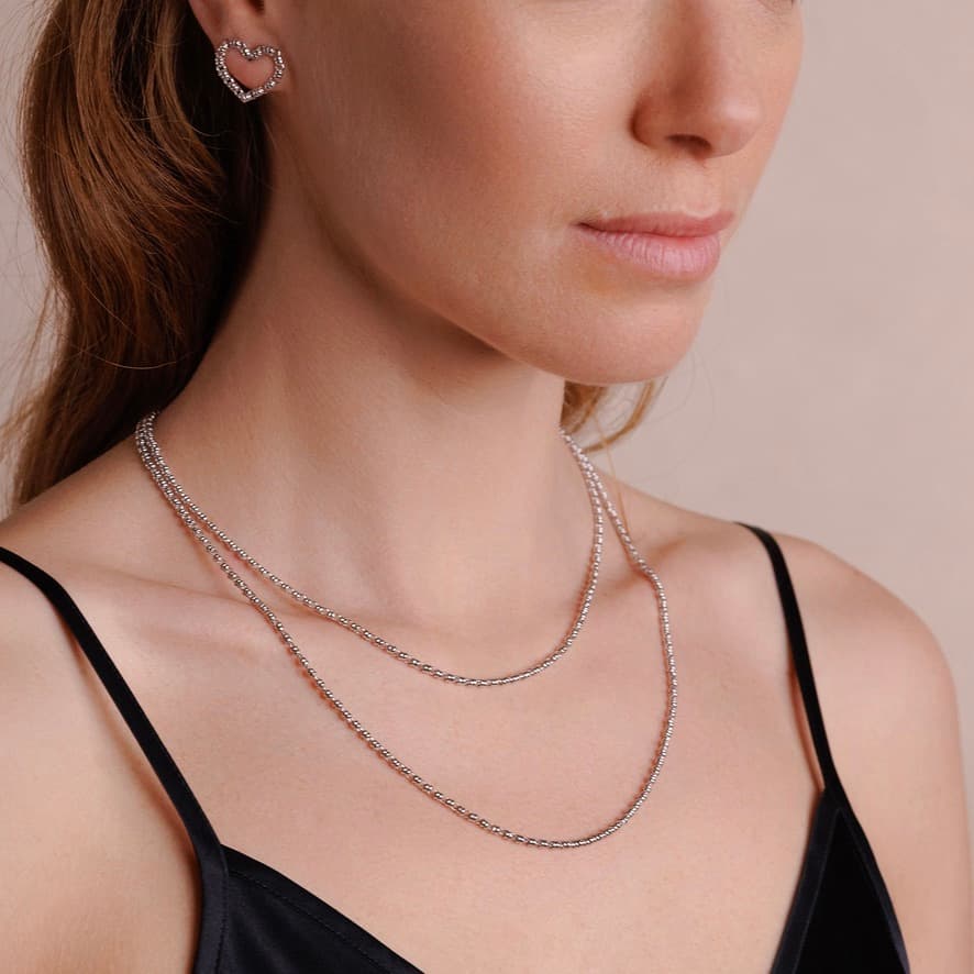 A model wearing two delicate, hand-crafted 2MM silver chains in two different lengths: a short, 16-18” silver chain necklace and a 20-22” silver necklace with matching silver heart earrings - all silver necklaces and earrings are crafted by DelBrenna Italian Jewelry designers in Tuscany. 