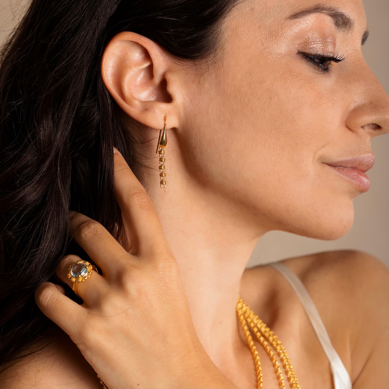 A model holding her hair back to show four gold chains with matching long gold chain earrings and a gold ring in the same iconic chain design around a semi-precious gemstone. All hand-crafted Italian jewelry is made by DelBrenna Italian Jewelers in Tuscany. 