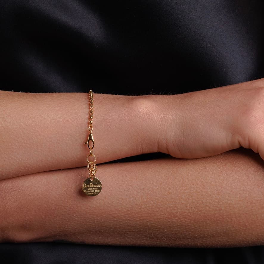 A model wearing a delicate gold chain bracelet with a small circular gold charm and lobster clasp all in 24K yellow gold finish over 925% sterling silver. The gold bracelet is designed from the iconic DelBrenna Links collection - Italian jewelry designs hand-crafted in Tuscany. 