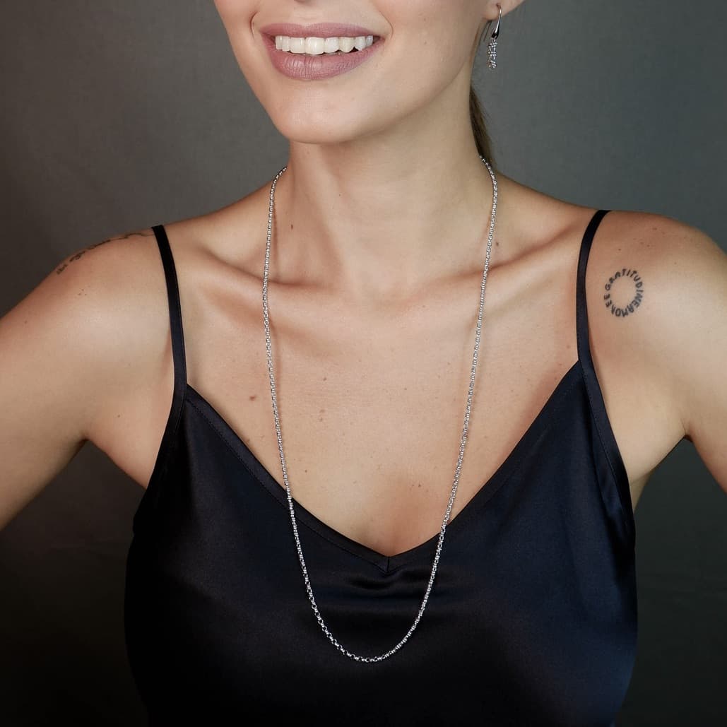 A front-facing, closeup view of a model wearing a long (30-inch) silver necklace with matching silver earrings. The necklace and earrings are a delicate 2MM version of the iconic silver chain designed by DelBrenna Italian jewelry designers in 1974 in Tuscany. 