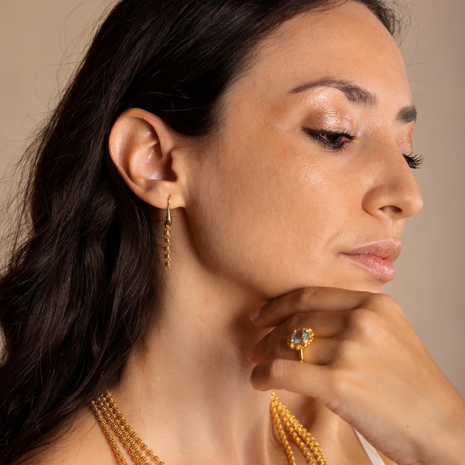 A model wearing four gold chains with matching long gold chain earrings and a gold ring in the same iconic chain design around a semi-precious gemstone. All hand-crafted Italian jewelry is made by DelBrenna Italian Jewelers in Tuscany. 