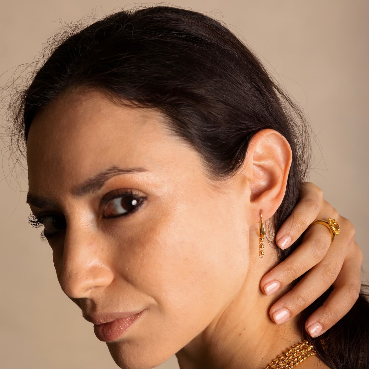 A model wearing four gold chains with matching gold chain earrings and a gold ring in the same iconic chain design around a semi-precious gemstone. All hand-crafted Italian jewelry is made by DelBrenna Italian Jewelers in Tuscany. 