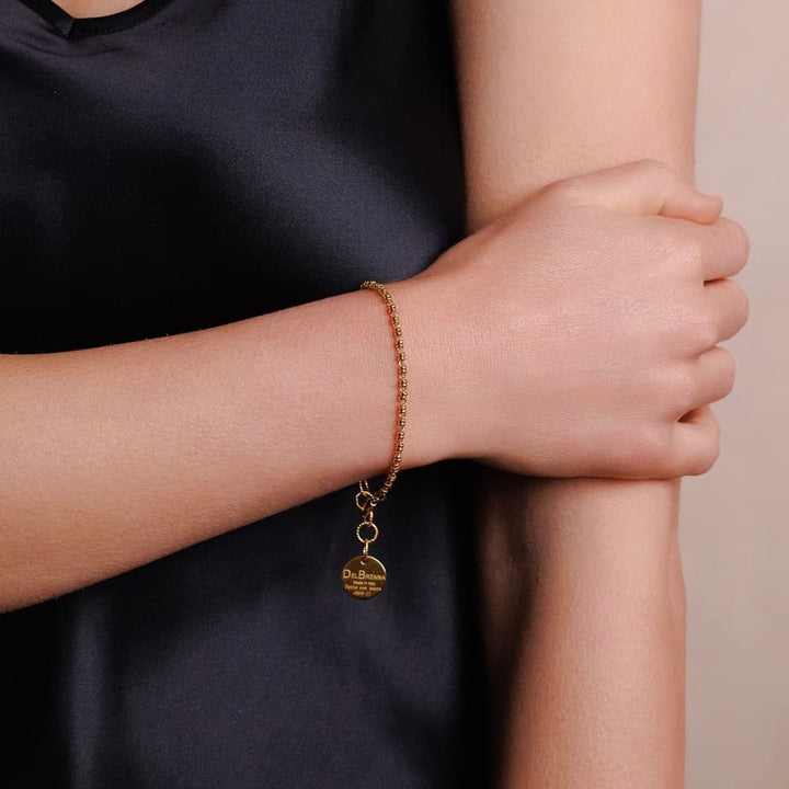 A closeup of a model wearing a delicate gold chain bracelet with a small circular gold charm and lobster clasp all in 24K yellow gold finish over 925% sterling silver. The gold bracelet is designed from the iconic DelBrenna Links collection - Italian jewelry designs hand-crafted in Tuscany. 