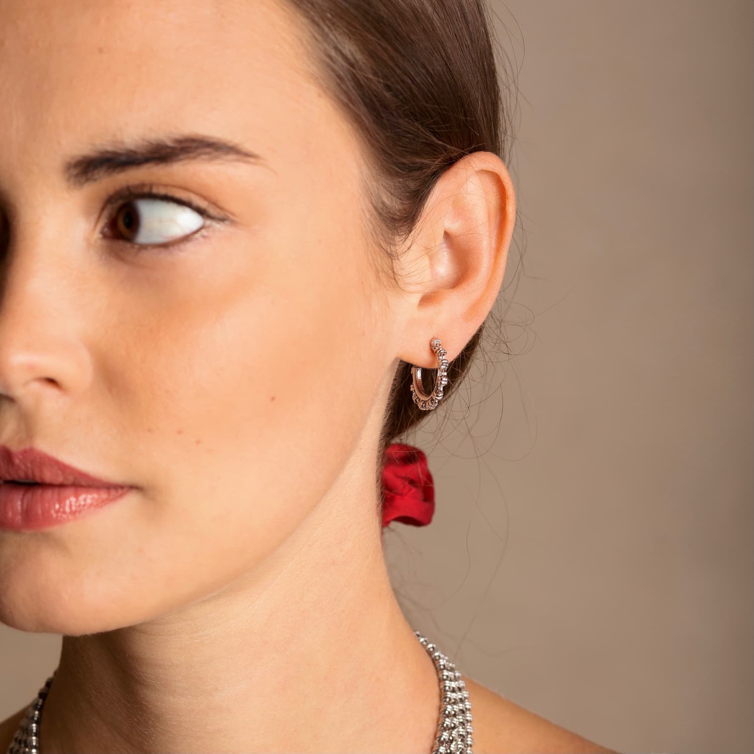 A closeup of a model wearing silver hoop earrings designed and hand-crafted by DelBrenna Italian Jewelers in Tuscany. The earrings and necklace shown here are designed based on the iconic Links collection of DelBrenna silver chains, necklaces, rings, and bracelets. 