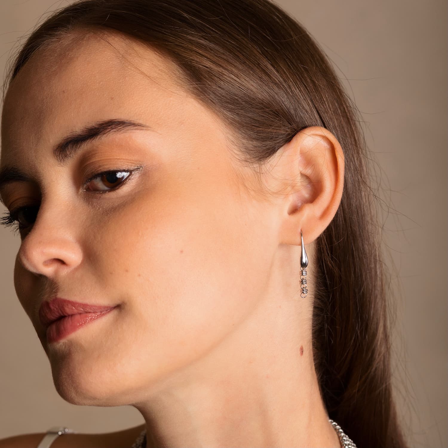 A model tilting her head while wearing silver chain earrings designed and hand-crafted by DelBrenna Italian Jewelers in Tuscany. The earrings and necklace shown here are designed based on the iconic Links collection of DelBrenna silver chains, necklaces, rings, and bracelets. 