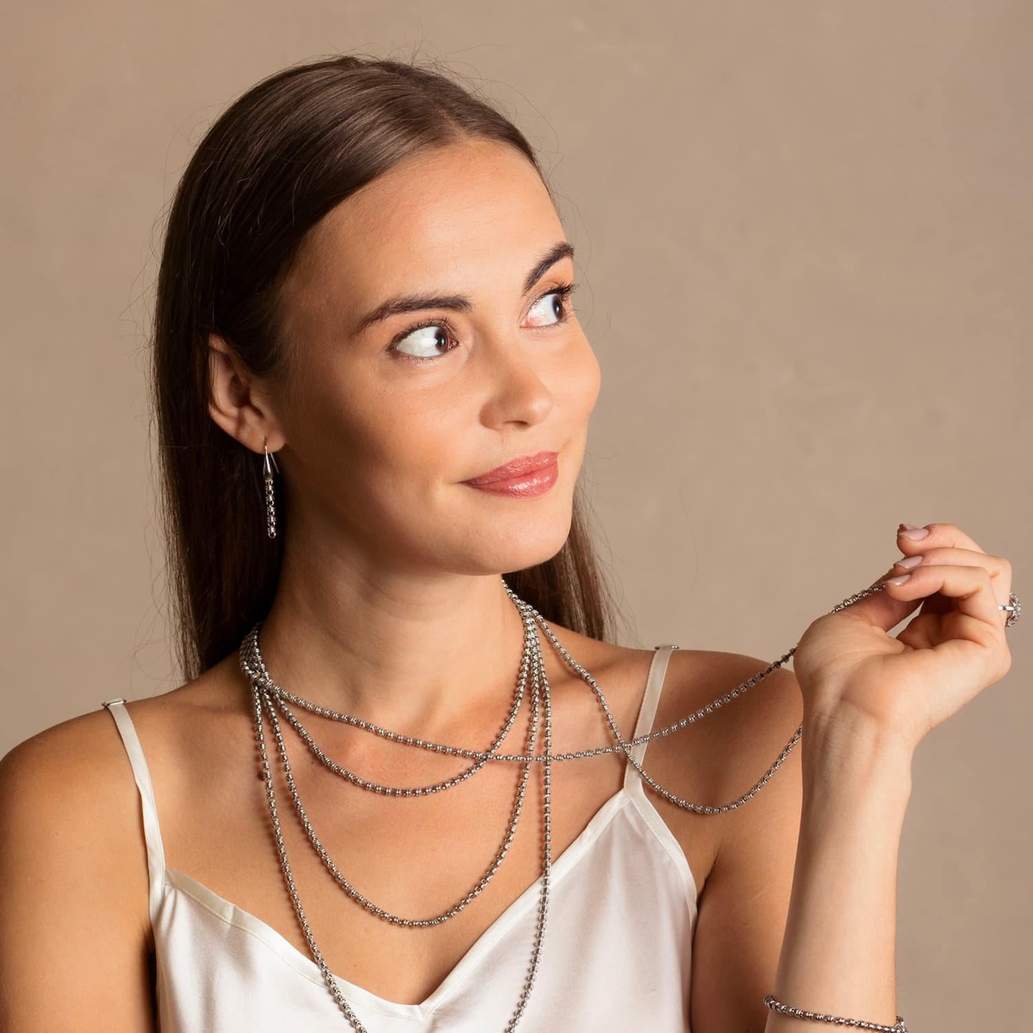 A model wearing long silver chain earrings, four silver chain necklaces, and a silver bracelet designed and hand-crafted by DelBrenna Italian Jewelers in Tuscany. The earrings are designed based on the iconic Links collection of DelBrenna silver chains, necklaces, rings, and bracelets.