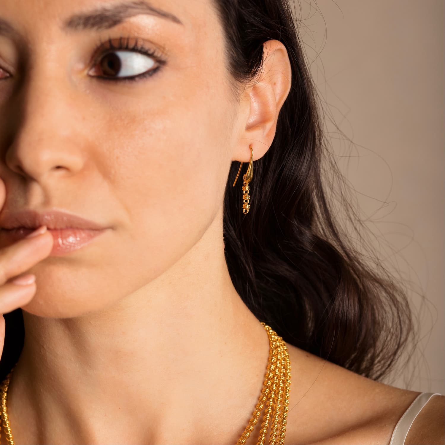 A model wearing four gold chains with matching gold chain earrings in the same iconic chain design around a semi-precious gemstone. All hand-crafted Italian jewelry is made by DelBrenna Italian Jewelers in Tuscany. 